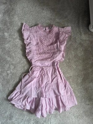 Rosa/lila playsuit - Så fin playsuit med spets, ser ut som en klänning med öppning i ryggen. Köpt för ca 600kr från en butik i Spanien. Står M/L men sitter som en S. Endast använd vid ett tillfälle därmed superfint skick!🩷🌸 Jag är 178 för referens.