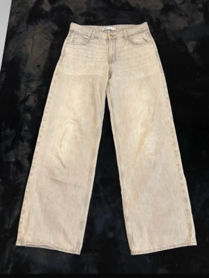 Grå vida jeans från Zara - Säljer ett par grå jeans från Zara med riktigt breda ben och klassisk femficksmodell. Jeansen har hög midja, gylf med knapp och dragkedja samt bälteshällor. Materialet är denim i bomull och färgen är ljusbeige med en lätt tvättad look.
