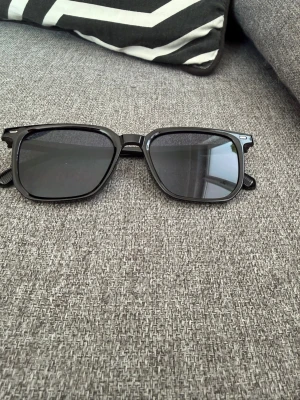 Svarta fyrkantiga solglasögon - Snygga svarta solglasögon från Secrid med fyrkantiga bågar och mörka linser. Perfekt för dig som vill ha en stilren och modern look. Bågarna är tillverkade i syntetmaterial och passar till alla som gillar klassisk design.