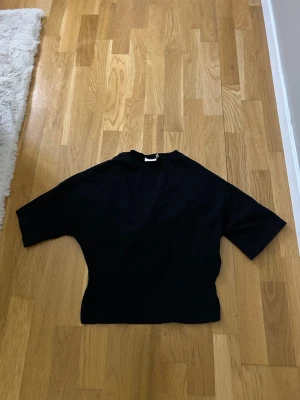 Svart topp med knytband - Snygg svart topp med knytband i midjan och korta ärmar. Toppen har en enkel och stilren design som passar till många olika looks. Super snygga till vardags och fest.