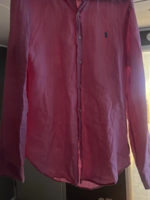 Rosa linneskjorta från Polo Ralph Lauren - Säljer en snygg rosa skjorta från Polo Ralph Lauren i slim fit. Skjortan är tillverkad i linne, har långa ärmar, klassisk krage och knappar framtill. Ikoniska Polo-loggan broderad på bröstet. Perfekt för dig som gillar stilrena plagg med färg. (skrynklig för att det är linne, går att stryka)