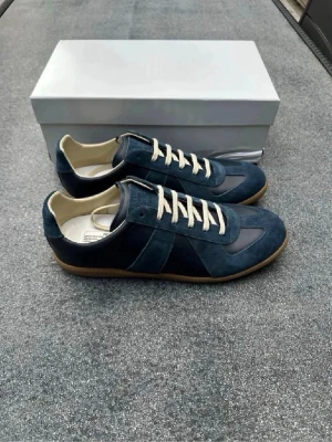 Maison Margiela gats blå - Snygga blå sneakers med ovandel i mocka och läderdetaljer. Skorna har vita snören, beige innersula och klassisk gummisula. Perfekta för dig som gillar stilrena och tidlösa sneakers med en modern twist. Hojta bara till för mer bilder. 0bs; lnte 0rglnal, men mycket bra kvalitet 