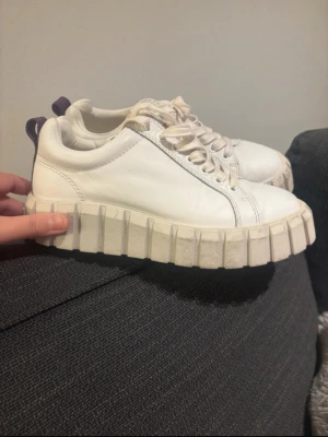Vita chunky sneakers från Eytys - Säljer ett par vita chunky sneakers från Eytys med kraftig, räfflad platåsula och lila hälflik. Skorna är i läder och har vita skosnören. Perfekta för dig som gillar statement-skor och vill ha något som sticker ut.