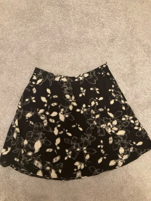 Svart blommig kjol!  - Fin svart kjol med vita blommor på och dragkedja på sidan. Aldrig använt, från Åhléns i storlek 36! 