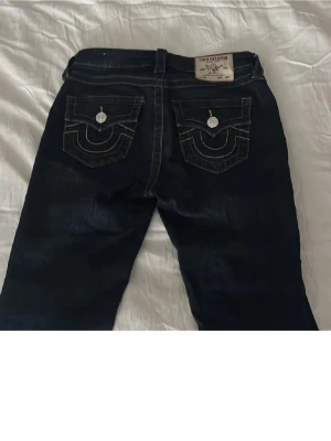 True Religion bootcut jeans mörkblå - Säljer pågrund av att dom inte blivit använda. Dom är lite söndertrampade längst ner för dom var lite för långa. Säljer ett par mörkblå True Religion jeans, modell BECCA Mid Rise Bootcut. Jeansen har snygga kontrastsömmar och ikoniska fickdetaljer med vita knappar bak. Klassisk bootcut passform och tillverkade i denim. Perfekta för en trendig och avslappnad stil.
