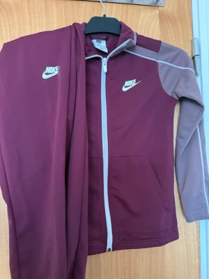 Nike set  - vinröd träningsset från Nike med logga på både jacka och byxa.Materialet är mjukt och stretchigt, perfekt för träning Storlek 128-137