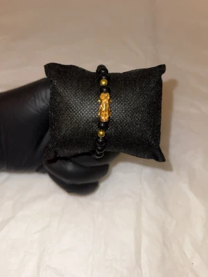 Svart pärlarmband med gulddrake - Coolt armband med svarta pärlor och guldfärgade detaljer. Mitt på sitter en liten drake i guldfärg som ger armbandet en unik och trendig look. Perfekt accessoar för dig som gillar detaljer med attityd. Elastiskt band gör det enkelt att ta på och av.