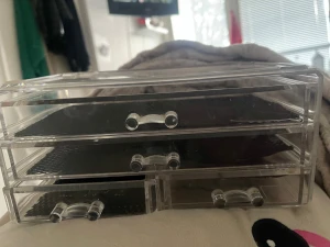 Transparent sminkförvaringslåda - Praktisk sminkförvaringslåda i transparent akryl med tre lådor och svarta halkskyddsmattor. Perfekt för att organisera borstar, smink eller små tillbehör. Modern och stilren design som passar på sminkbordet eller i badrummet.