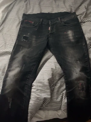 Svarta distressed jeans från Dsquared2 - Snygga svarta jeans från Dsquared2 med slitna detaljer, hål och blekta partier. Jeansen har en rak passform och klassisk femficksdesign. Tillverkade i denim med coola färgstänk och trendig look.