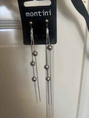 Silvriga långa örhängen Montini - Säljer ett par silvriga långa örhängen från Montini. Örhängena har tunna kedjor med små metallpärlor i rad som ger en stilren och trendig look. Perfekta för dig som gillar minimalistiska accessoarer med lite extra detalj.