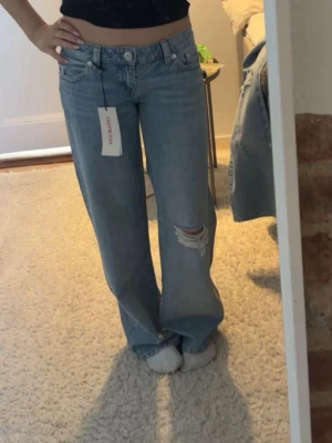 Ljusblåa vida jeans från Gina Tricot - Säljer ett par ljusblåa jeans från Gina Tricot med lös passform och låg midja. Helt nya, har kvar prislappen. Jeansen har slitningar på ena knät.