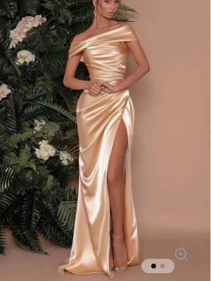 Champagnefärgad balklänning i satin - Elegant offshoulder långklänning i champagnefärgad satin med draperad midja och hög slits från VioletAurora. Aldrig använd!Klänningen har en figurnära passform och glänsande material som ger en lyxig känsla. Perfekt för dig som vill sticka ut på bal eller fest.