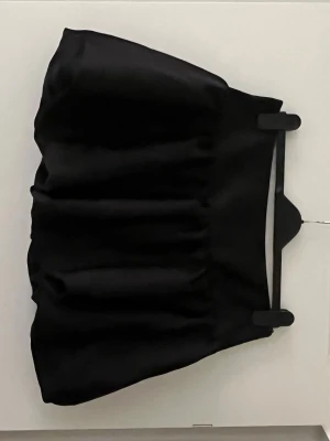 Svart bubblig kortkjol i satin - Supersnygg svart kortkjol med bubblig effekt och bred midja. Kjolen har en glansig satinlook som ger en lyxig känsla och passar perfekt till en trendig outfit. Enkel att matcha med både crop tops och stickade tröjor.