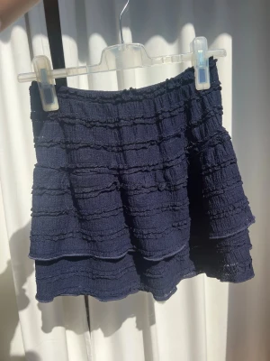 Mörkblå volangkjol - Supersöt mörkblå kortkjol med volanger och struktur i tyget. Har resår i midjan så den passar flera storlekar men är egentligen storlek M🥰 