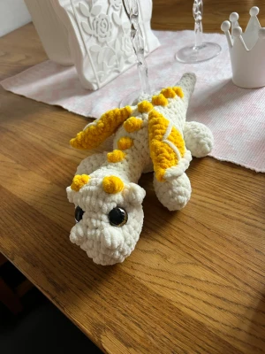 Vit drake med gula detaljer - Denna urgulliga drake längtar efter sitt för alltid hem💛🫶🏼✨ Det är en vit drake med gula detaljer, virkat med mjukt garn från Hobbii som heter Baby Snuggle🫶🏼 Den har hårda guldiga ögon som inte går att ta av, sitter som bergen✨💛 Den är cirka 30 cm lång💛