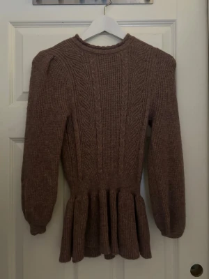 Stickad brun peplumtröja från ONLY - Säljer en brun stickad tröja från ONLY med peplumdetalj nedtill och puffade axlar. Tröjan har kabelstickat mönster framtill, rund halsringning och långa ärmar med ribbade muddar. Ny pris 250kr