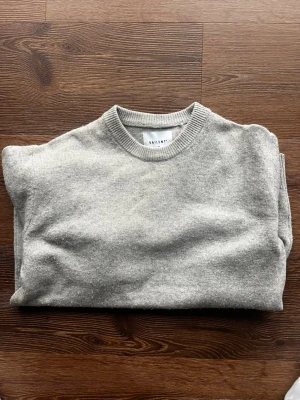 Ljusgrå stickad tröja från Vailent - En stilren ljusgrå stickad tröja från Vailent med rund halsringning och ribbade muddar vid ärmslut och nederkant. Tröjan har en klassisk passform och är tillverkad i mjukt material som passar perfekt till lager på lager.