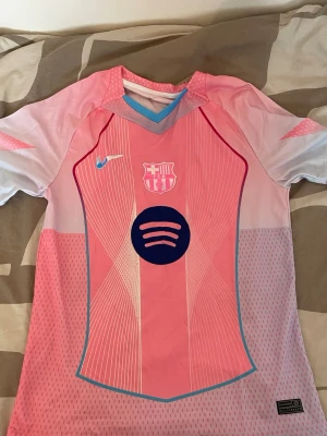 FC Barcelona rosa matchtröja Nike S - Snygg FC Barcelona matchtröja i rosa och ljusblått från Nike. Tröjan har klubbmärke och Spotify-logga på bröstet, samt Nike-logga. Tillverkad i lätt och ventilerande material, perfekt för fotboll eller träning. Modern design med korta ärmar och V-ringning.