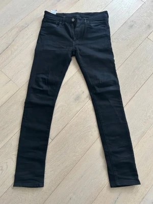 Svarta jeans från Levi's - Säljer ett par svarta jeans från Levi's med klassisk femficksdesign och knappgylf. Jeansen har en smal passform och är tillverkade i ett stretchigt material för extra komfort. Perfekta för dig som gillar en stilren och enkel look. Hör av er vid fler frågor, priset går att diskutera.