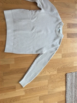 Beige stickad tröja från COS - Snygg beige stickad tröja från COS i relaxed fit. Tröjan har rund halsringning och ribbade muddar vid ärmslut och nederkant. Perfekt basplagg i garderoben och enkel att matcha med olika stilar.