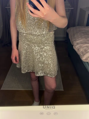 Glittrig silverkort kjol med paljetter - Säljer en glittrig kjol i silver med paljetter. Passar någon  som är 150 cm 