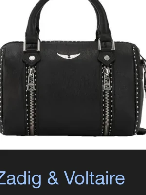 Svart handväska Zadig & Voltaire - Cool svart handväska från Zadig & Voltaire i läder med silverfärgade detaljer, dubbla dragkedjor framtill och nitar längs fram. Jag undrar om någon vill byta väskan mot en i xs då denna är i S annars säljer jag den runt 2000