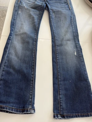 Blå bootcut jeans från Formarina med slitningar - Säljer ett par blå bootcut jeans med snygga slitningar och lätt tvättad look. Jeansen har klassisk femficksdesign och kontrastsömmar. Perfekta för dig som gillar en avslappnad men trendig stil.