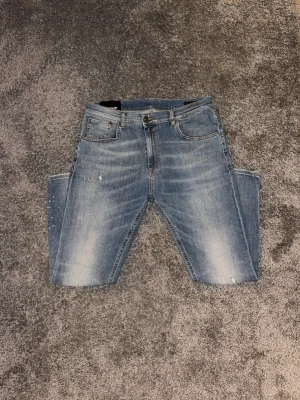 Ljusblå jeans med slitningar från Dondup - Säljer ett par ljusblå jeans från Dondup med tvättade detaljer och små slitningar framtill. Klassisk femficksmodell med slim-fir passform och normal midja. Jeansen har subtila färgstänk och kontrastsömmar för en trendig look. Perfekta för dig som gillar en avslappnad stil.