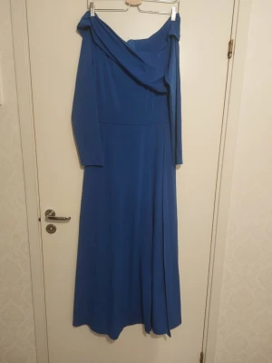 Blå byxdress med kjol med offshoulder - Snygg blå byxdress med kjol  med offshoulder-design och långa ärmar. Byxdress  har en elegant drapering vid axlarna och ett stilrent, enfärgat tyg som faller fint. Perfekt för dig som vill sticka ut med en klassisk och trendig look.