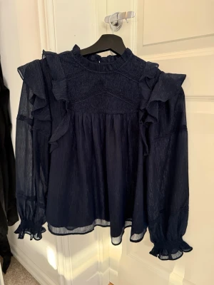 Mörkblå volangblus med lång ärm - Snygg mörkblå med glitter blus från Gina tricot young med volangdetaljer på axlar och ärmar. Använd 2 gånger så i ny skick! Storlek 146/152 men passar lite större. Perfekt till resturang men också vardag. Bara att höra av sig vid frågor💓💓