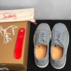 Gråa sneakers från Christian Louboutin - Snygga blåa sneakers från Christian Louboutin med ovandel i textil och vita gummisulor. Skorna har klassisk låg profil, matchande blå skosnören och beige innersula med diskret branding. Perfekta för en clean och stilren look.