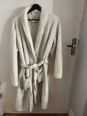 Mysig vit fleece morgonrock - Supermjuk och fluffig vit morgonrock i fleece med långa ärmar, två fickor och knytskärp i midjan. Perfekt för att chilla hemma och hålla sig varm under kyliga dagar. Klassisk omlottmodell med skön krage. Fickorna är lite trasiga i botten, men lätt att sy. Passar både XS-M. Har bundle rabatt! 