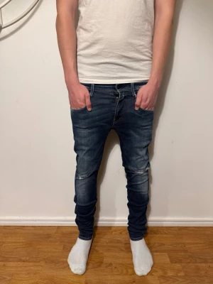 Blå slimfit jeans från replay - Snygga blå slimfit jeans från replay med slitningar vid knäna och lätt tvättad look. Jeansen har klassisk femficksmodell, låg midja och bra passform som sitter bra längs benen. Jeansen är i storlek w28 l30. Perfekta för en avslappnad och trendig stil. Pris kan diskuteras✅