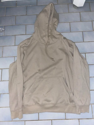 Beige hoodie med magficka - Snygg beige hoodie med huva och dragsko. Klassisk modell med stor magficka framtill och ribbade muddar vid ärmslut och nederkant. Perfekt för en avslappnad och stilren look.