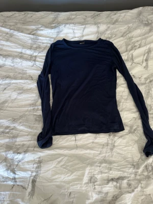 Mörkblå långärmad tröja - En enkel och stilren mörkblå långärmad tröja med rund hals. Tröjan har en smal passform och är tillverkad i ett tunt, mjukt material som känns skönt mot huden. Perfekt att bära som lager eller för en clean look.
