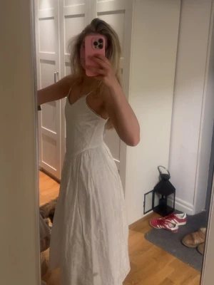 Vit långklänning med spetsdetaljer - Säljer en vit långklänning med tunna axelband och v-ringad hals.  Perfekt för sommarens alla tillfällen, speciellt midsommar! Materialet känns luftigt och bekvämt. Helt ny med prislapp kvar.