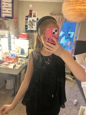 Svart ärmlös blus med volang - Säljer en svart, flowy ärmlös blus med volangdetaljer. Toppen har en lös passform och faller snyggt över kroppen. Perfekt att styla med smycken och jeans för en trendig look.