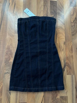 Mörkblå axelbandslös jeansklänning - Trendig mörkblå axelbandslös kortklänning i jeansmaterial med dragkedja i sidan, Alldrig använd och prislappen sitter kvar ! 