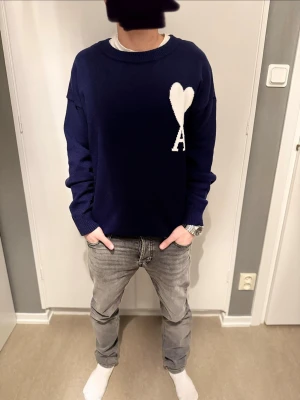 Marinblå stickad tröja från Ami - Säljer en marinblå stickad tröja från Ami med vit hjärtformad A-logga på bröstet. Tröjan har rund hals, ribbade muddar och långärmad passform. Först till kvarn!!!
