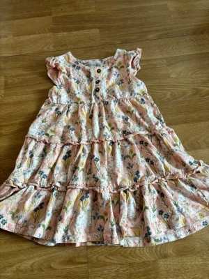 Klänning med kaniner på stl 92 - Söt klänning i ljusrosa med blommigt mönster och volanger. är tillverkad i mjuk bomull. Perfekt för sommarens varma dagar.