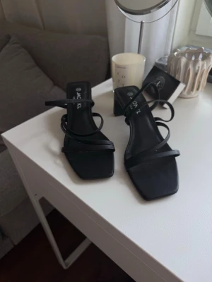 Svarta strappy sandaler från Monki  - Säljer ett par svarta sandaler från Monki med tunna remmar och fyrkantig tå. Sandalerna har en låg klack (5 cm). Tillverkade i konstläder.