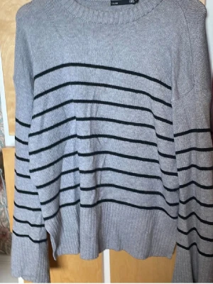 Grå stickad tröja med svarta ränder - Säljer en grå stickad tröja med svarta horisontella ränder. Tröjan har rund halsringning, långa ärmar och ribbade muddar vid ärmslut och nederkant. Perfekt för dig som gillar en enkel men snygg look.