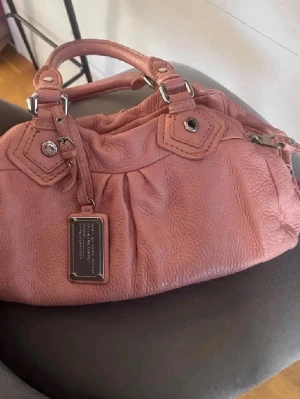 Marc by Marc Jacobs väska - Säljer en snygg rosa handväska från Marc by Marc Jacobs i mjukt läder. Väskan har silverfärgade metalldetaljer, dubbla handtag och ett coolt svartvitt innerfoder med logotypmönster. (Bilder från förra ägaren) hör gärna av er vid frågor.