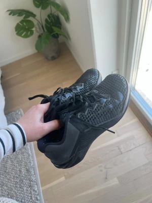 Svarta Nike Metcon  - Säljer ett par helsvarta Nike Metcon med mesh-ovandel och robust sula. Skorna har snörning och diskret Nike-logga på sidan. Perfekta för gymmet och vid träning. Lätta och ventilerande med sportig design.