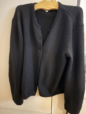 Svart kofta från H&M, M - En enkel svart kofta från H&M i storlek M. Koftan har rund halsringning, knäppning framtill och långa ärmar. Materialet är mjukt och lite fluffigt, perfekt för lager på lager. Passar till det mesta och är lätt att matcha. Som ni ser på sista bilden så har koftan ”knottrar”. Det är inget som påverkar användningen av den. 