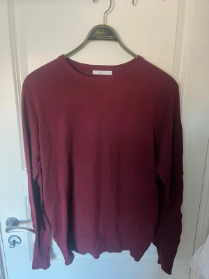 Vinröd stickad tröja - En enkel och stilren vinröd stickad tröja med rund halsringning och långa ärmar. Tröjan har ribbade muddar vid ärmslut och nederkant. Perfekt för lager på lager och passar till det mesta i garderoben.