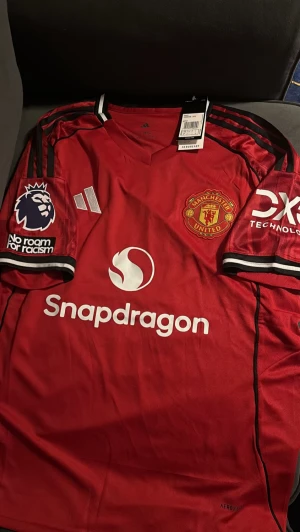Manchester United fotbollströja, bruno Fernandes #8 - Snygg röd Manchester United matchtröja f med svarta detaljer och klubbmärke på bröstet. Tröjan har sponsorloggor, Premier League-märke på ärmen och spelarnamn B. Fernandes med nummer 8 på ryggen. Tröjan är storlek L och har knappt hunnit komma till användning.