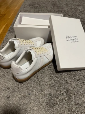 Maison Margiela vita - Säljer ett par vita sneakers från Maison Margiela. Skorna har en klassisk låg silhuett, vita skosnören och är tillverkade i en mix av läder och mocka. Perfekta för dig som gillar stilrena sneakers. Strl 44