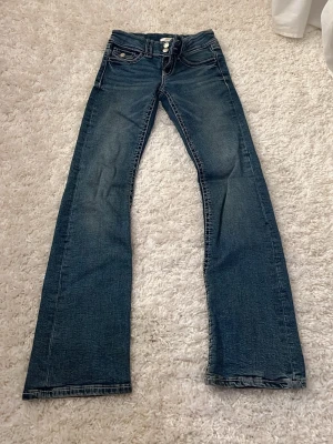 Blå bootcut jeans  - Säljer ett par blå bootcut jeans från gina young med dubbla silverknappar och klassiska fem fickor. Jeansen har kontrastsömmar. 