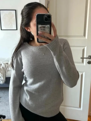 Ljusgrå stickad tröja - En stilren ljusgrå stickad tröja med rund halsringning och ribbade muddar vid ärmslut och nederkant. 